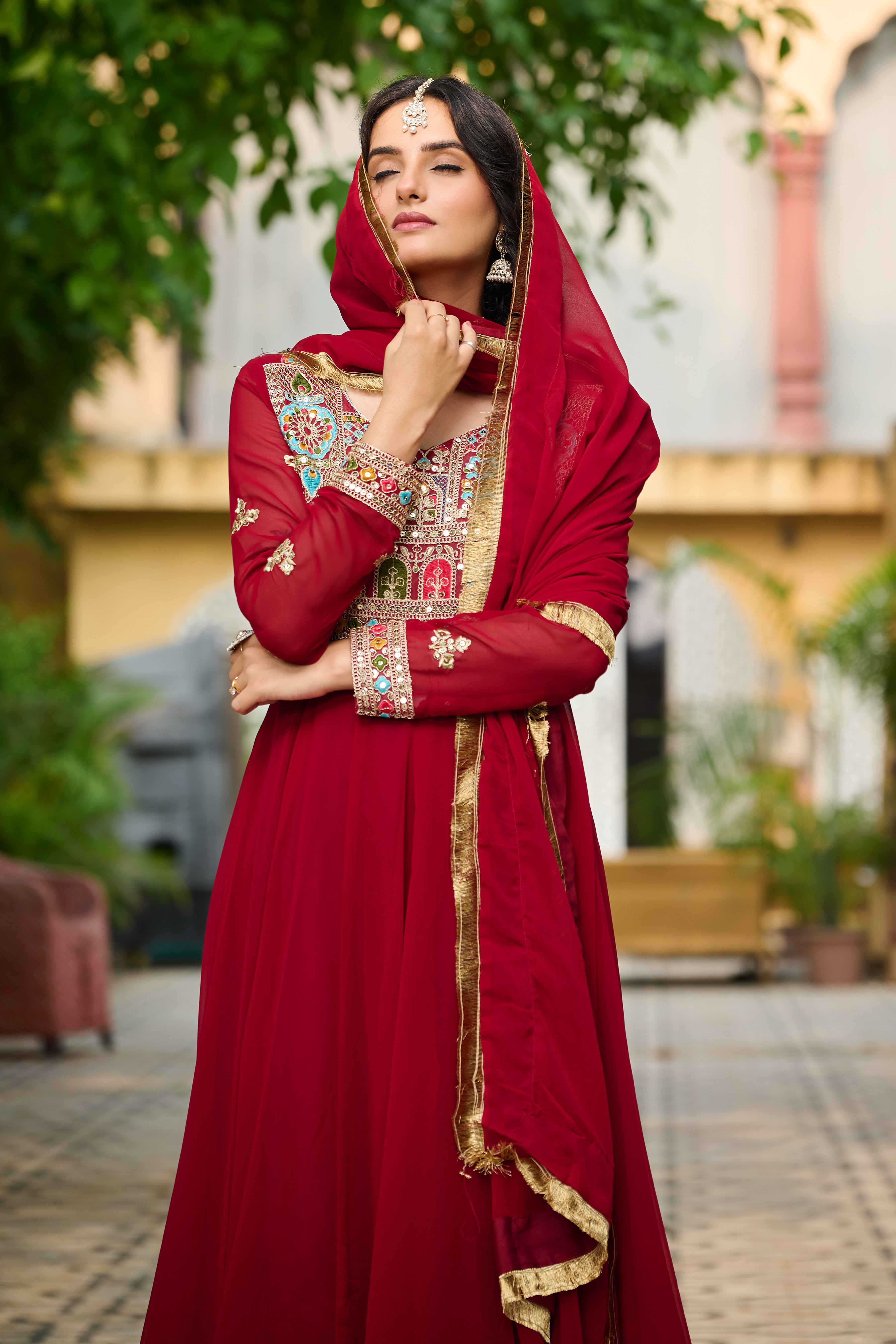 Woman in a red traditional outfit with gold details outdoors.