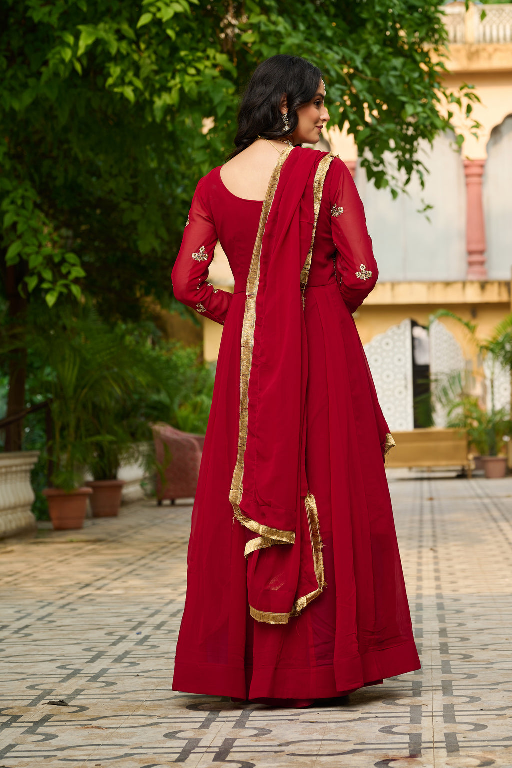 Woman in a red traditional outfit with gold details standing outdoors.