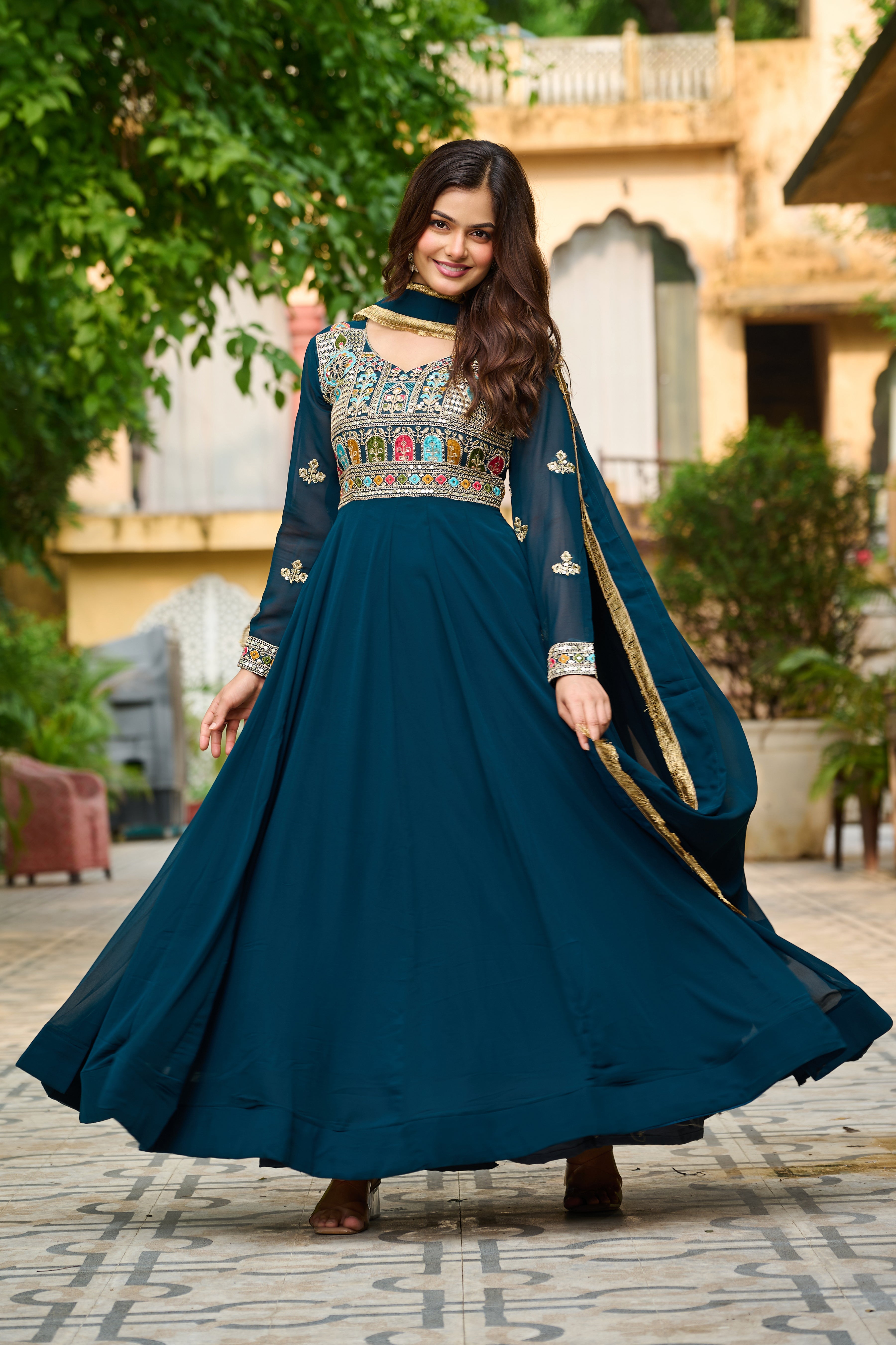 Woman in a traditional blue dress with intricate patterns standing outdoors.
