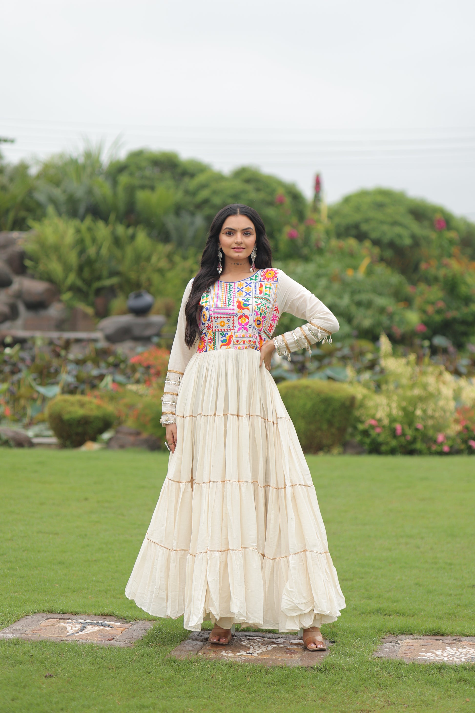 Woman in a colorful dress standing in a garden with greenery and a pond in the background