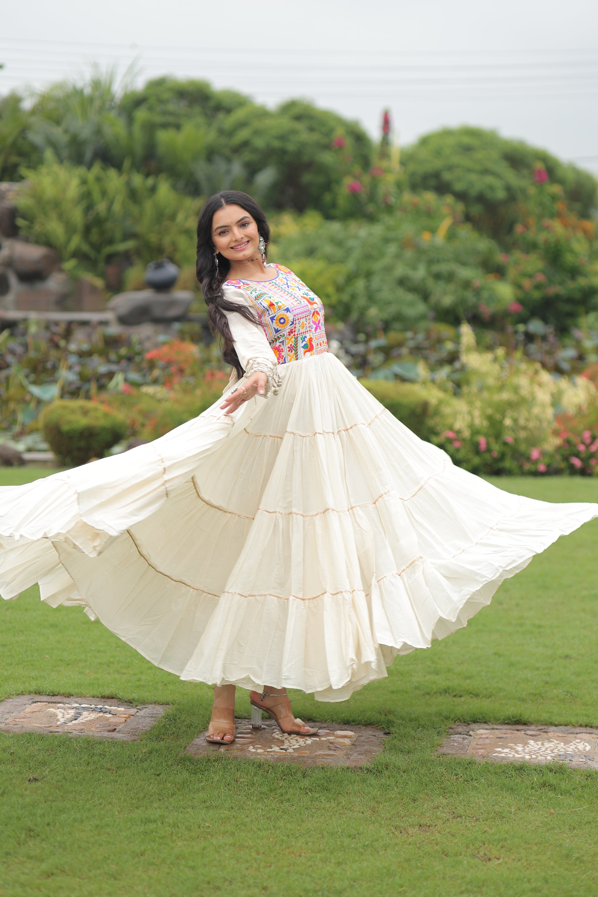 Woman in a white dress with a colorful top standing on grass with a garden background