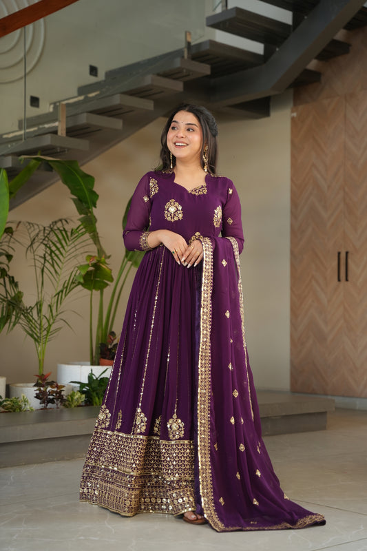 Woman in a purple traditional outfit with gold details standing indoors.