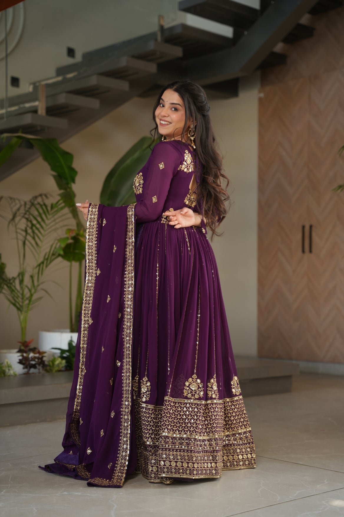 Woman wearing a purple traditional outfit with gold embroidery indoors.