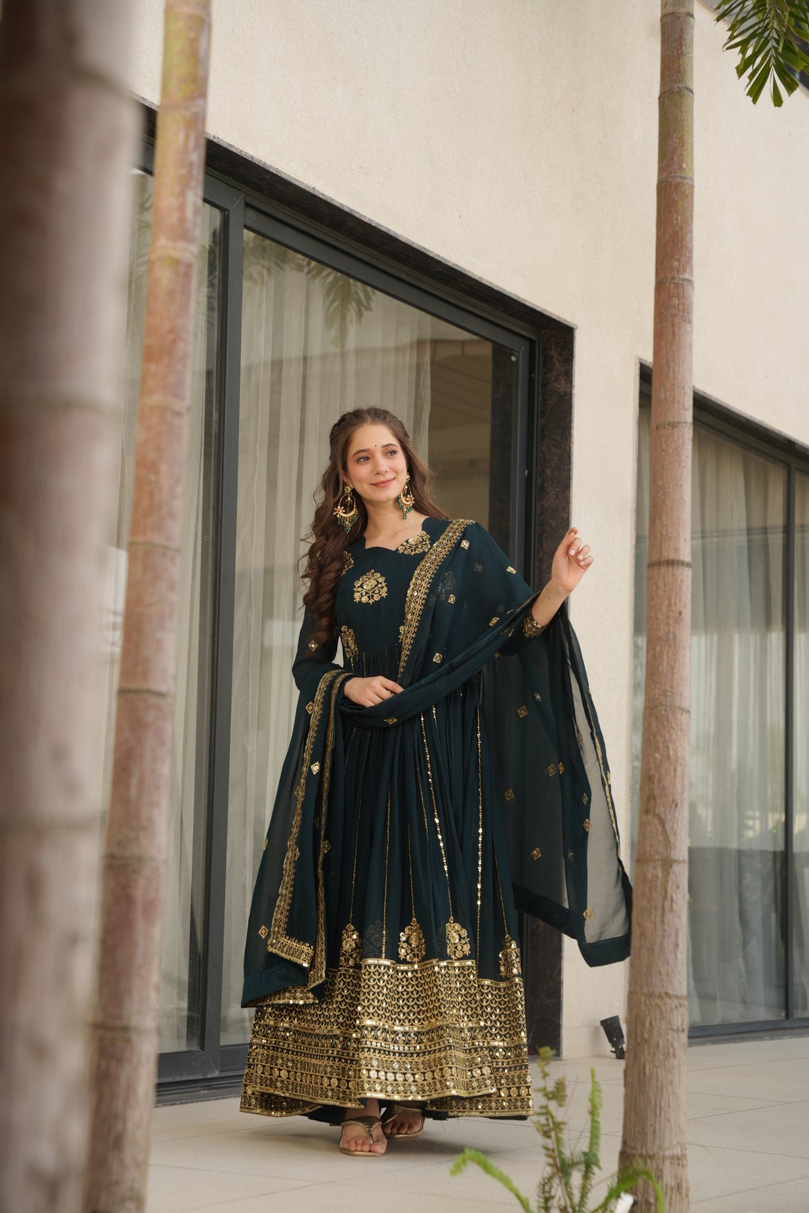 Woman in a dark blue traditional outfit with gold embroidery standing indoors.