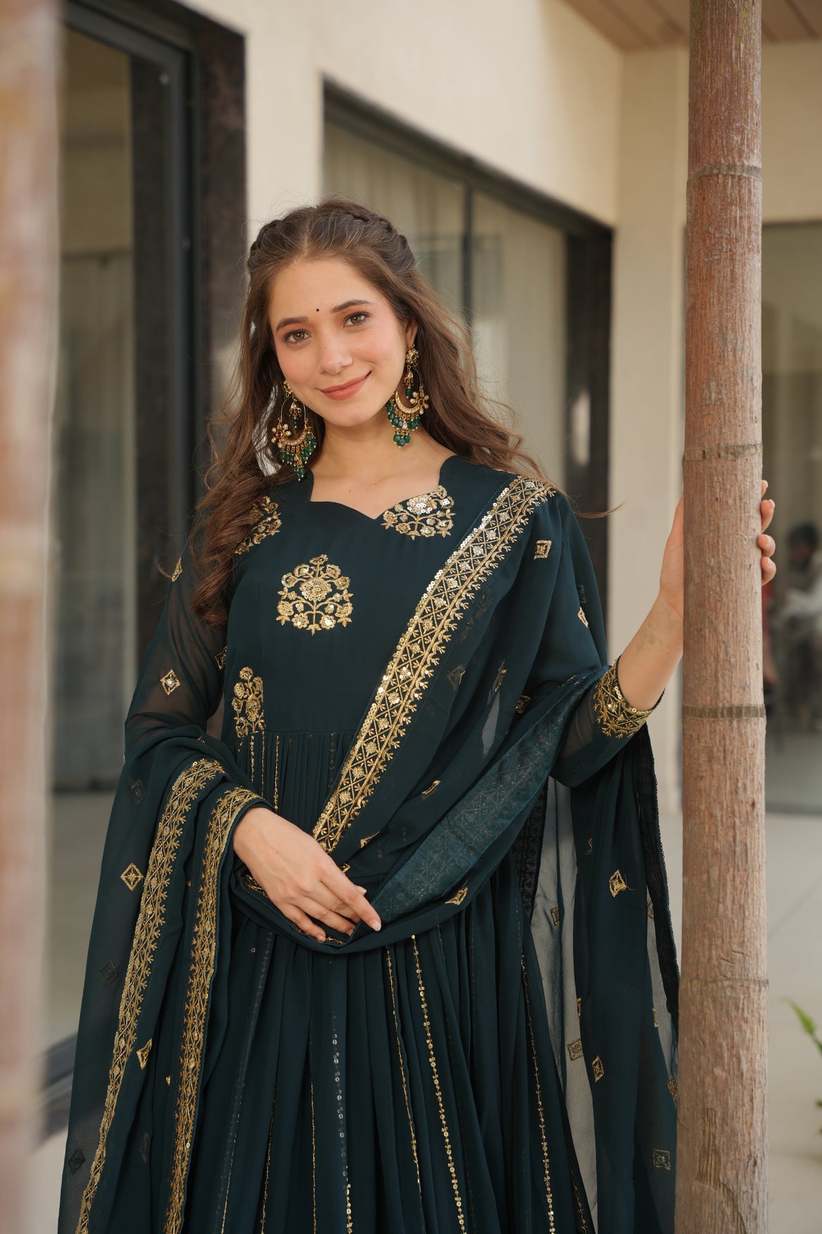 Woman wearing a dark green traditional outfit with gold embroidery indoors.
