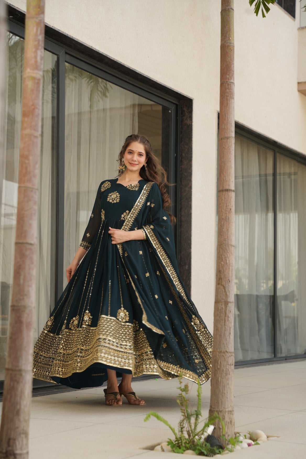 Woman in a dark blue traditional outfit with gold embroidery standing in front of a mirror.