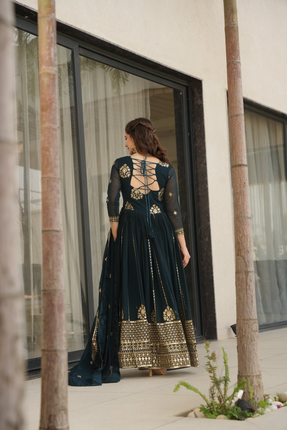 Woman wearing a dark blue dress with gold embroidery standing in front of a mirror.