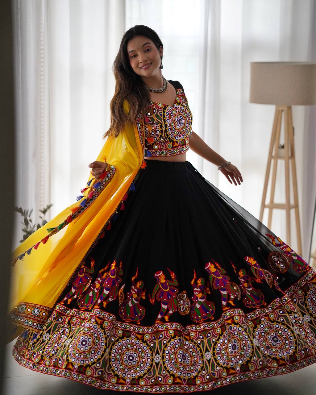 Woman wearing a traditional embroidered outfit with a yellow dupatta in a bright room.