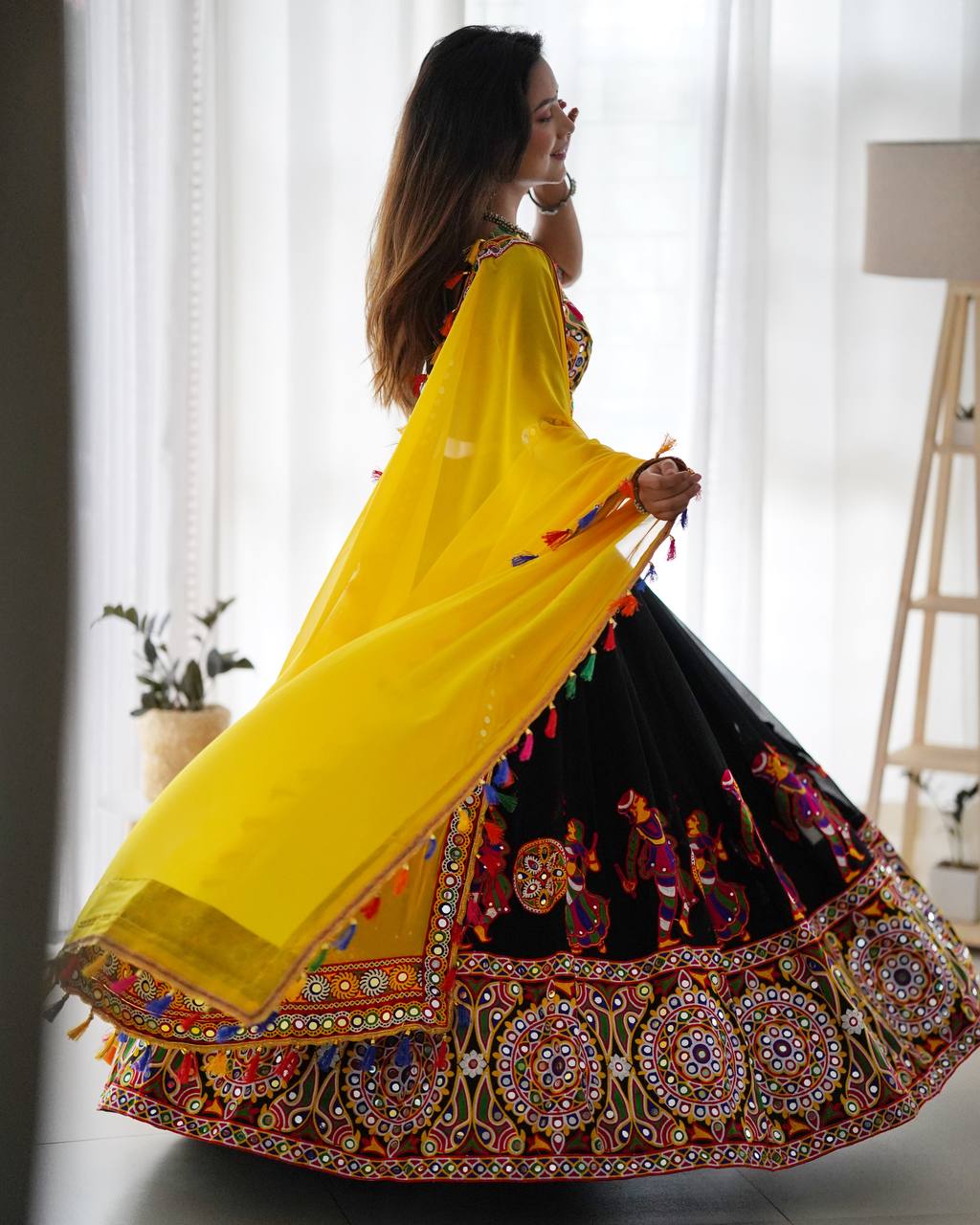 Woman in a colorful traditional outfit with a yellow dupatta in a room.