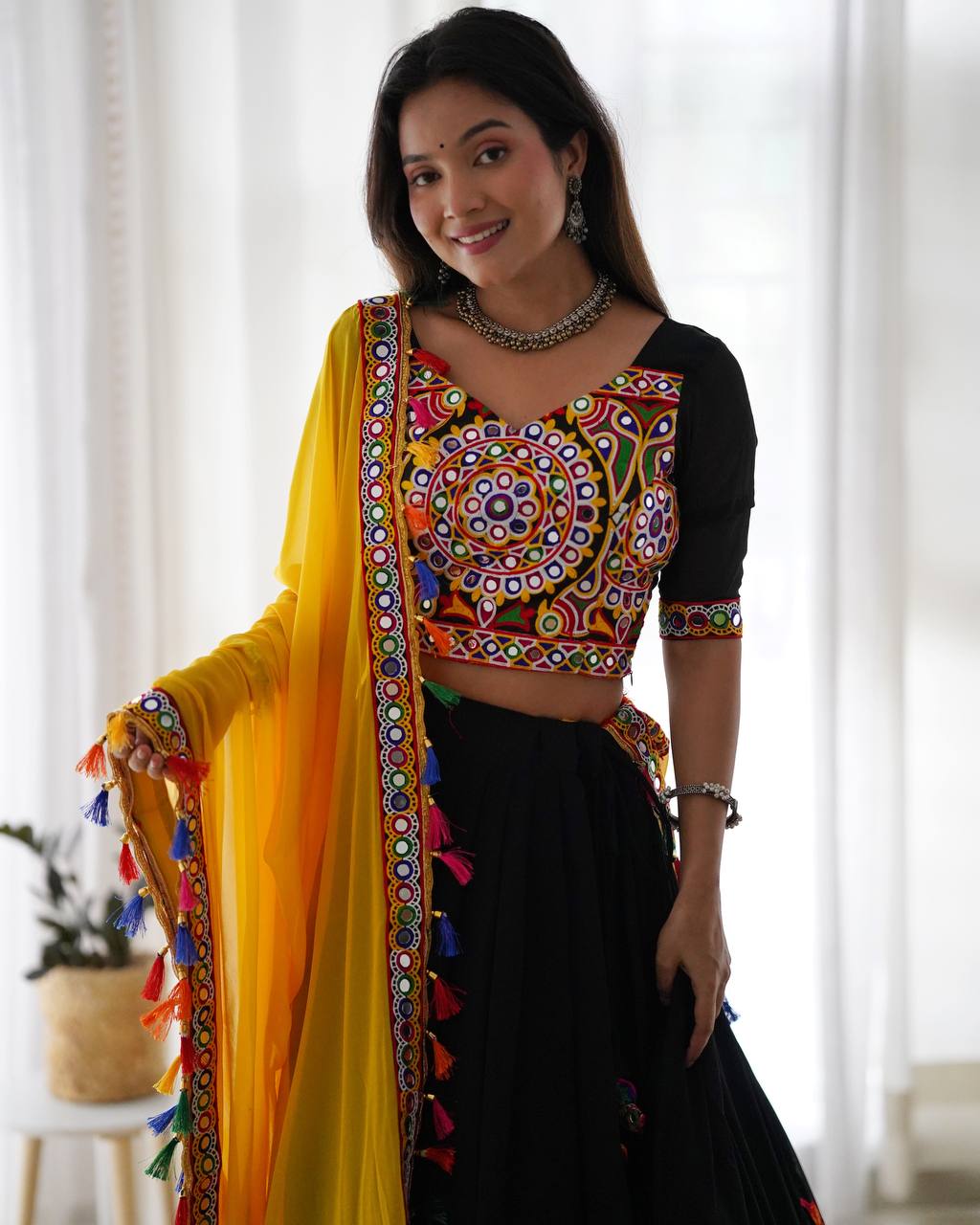 Woman wearing a colorful traditional outfit with a yellow dupatta in a bright room.