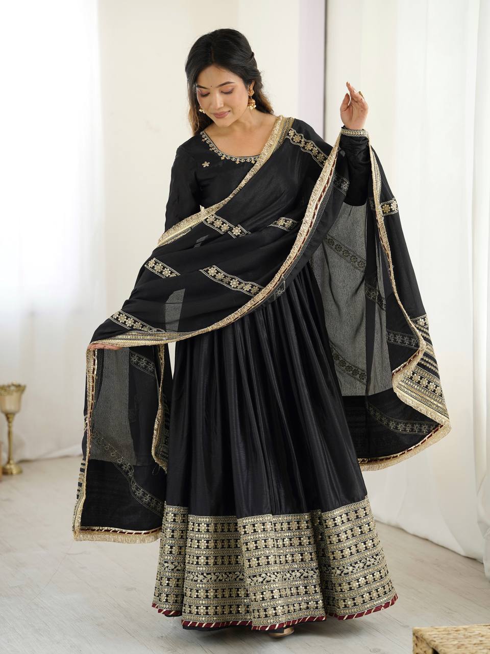 Woman wearing a black saree with gold embroidery in a minimal indoor setting