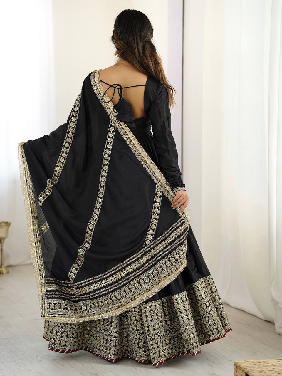 Woman wearing a black saree with gold embroidery in a minimal indoor setting