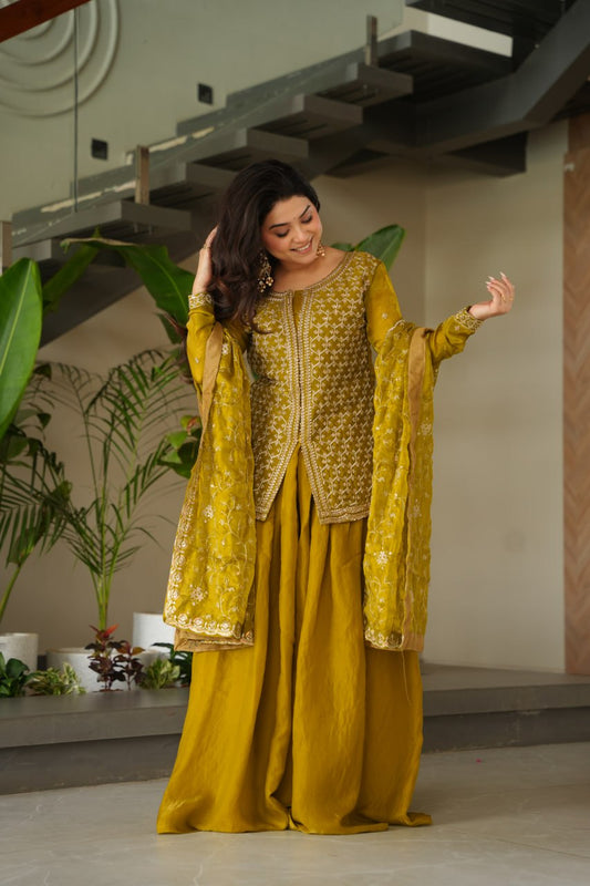 Woman in a yellow traditional outfit with intricate patterns standing indoors.
