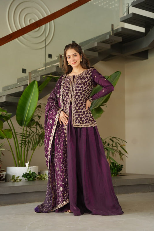 Woman in a traditional outfit standing indoors with plants and architectural elements in the background